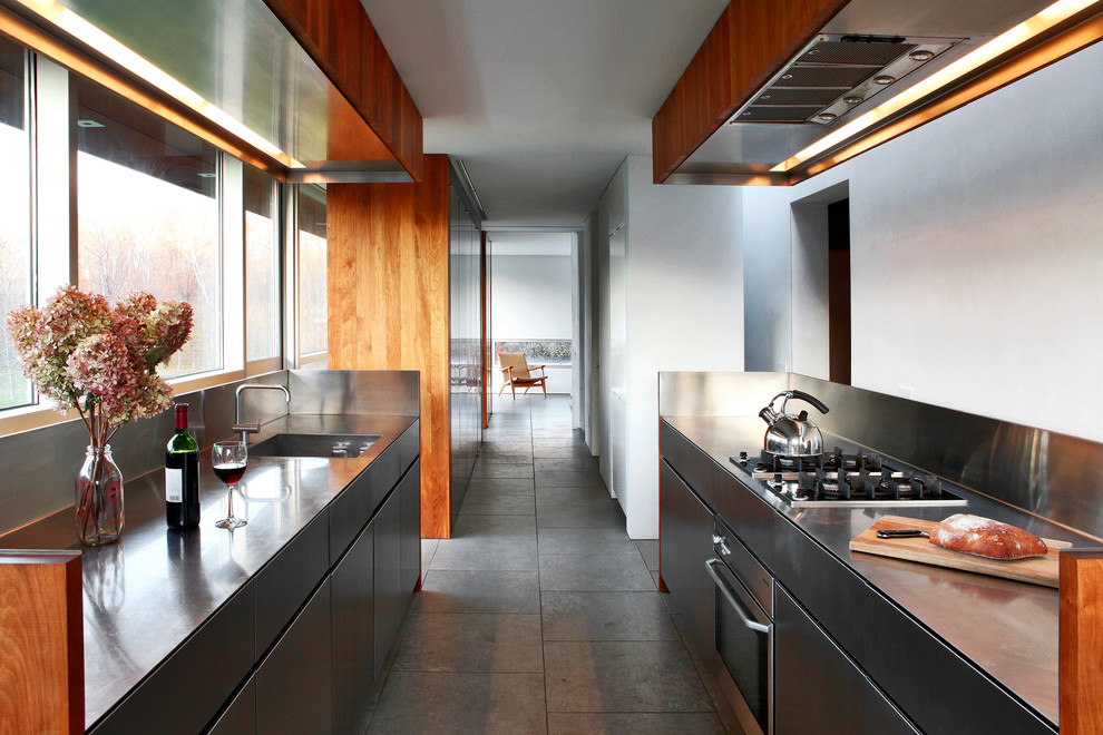 На фото: кухня в современном стиле с монолитной мойкой, плоскими фасадами и фартуком цвета металлик без острова