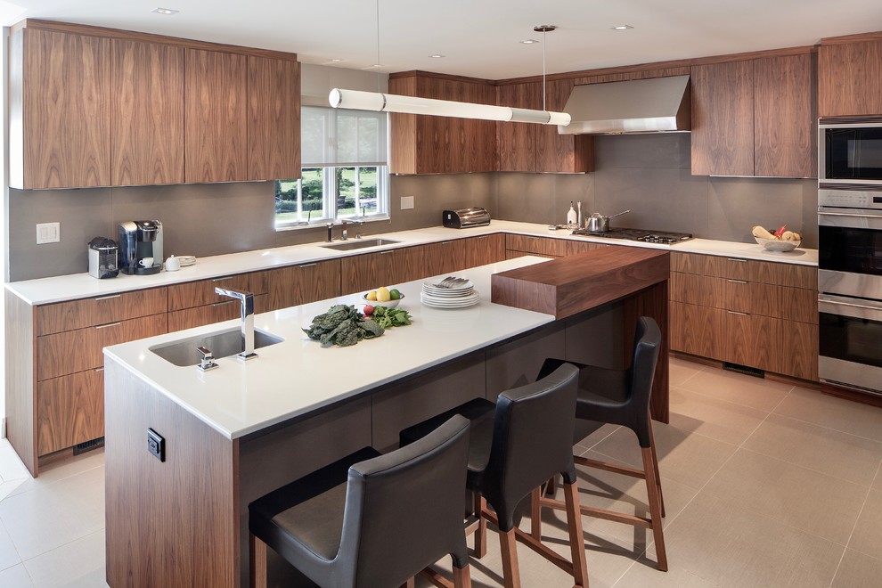 Modern inredning av ett kök, med en undermonterad diskho, släta luckor, skåp i mörkt trä, brunt stänkskydd, rostfria vitvaror och en köksö