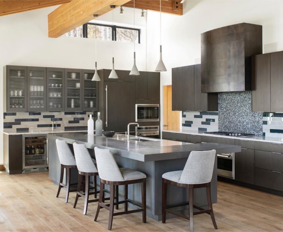 Inspiration for a large contemporary l-shaped kitchen/diner in Denver with a submerged sink, flat-panel cabinets, dark wood cabinets, blue splashback, ceramic splashback, stainless steel appliances, light hardwood flooring, an island, brown floors, white worktops and exposed beams.