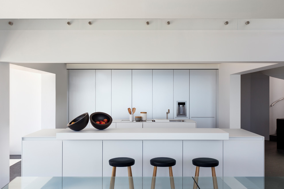 Cette image montre une cuisine parallèle design avec un placard à porte plane, 2 îlots, un plan de travail blanc et des portes de placard blanches.