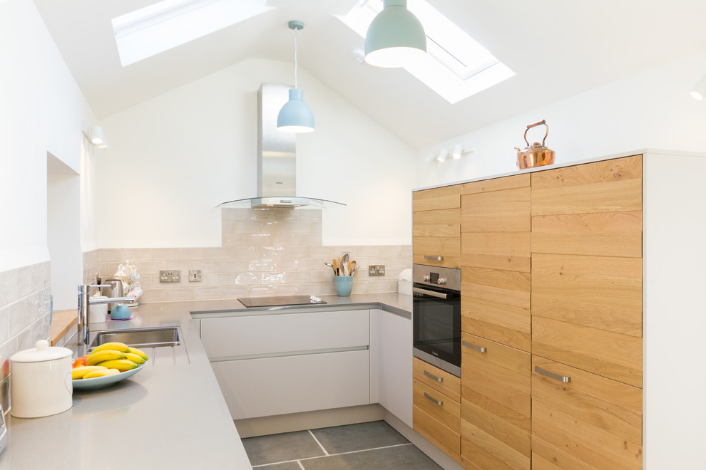 Small contemporary u-shaped kitchen in Devon with a double-bowl sink, flat-panel cabinets, light wood cabinets, beige splashback, metro tiled splashback, grey floors, grey worktops and stainless steel appliances.