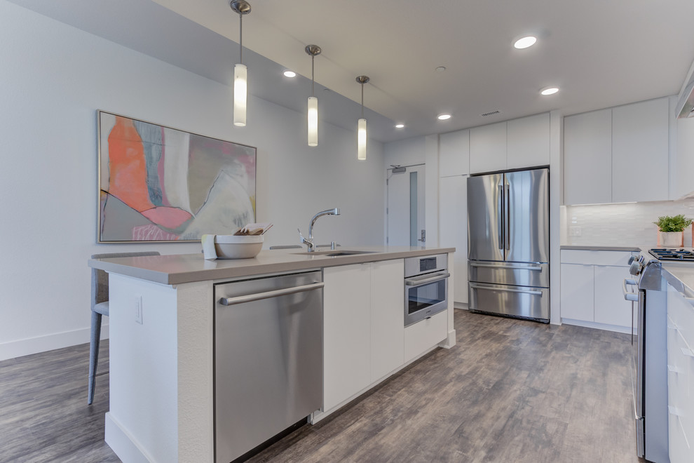 Example of a l-shaped light wood floor open concept kitchen design in San Francisco with flat-panel cabinets, white cabinets, white backsplash, stainless steel appliances and an island