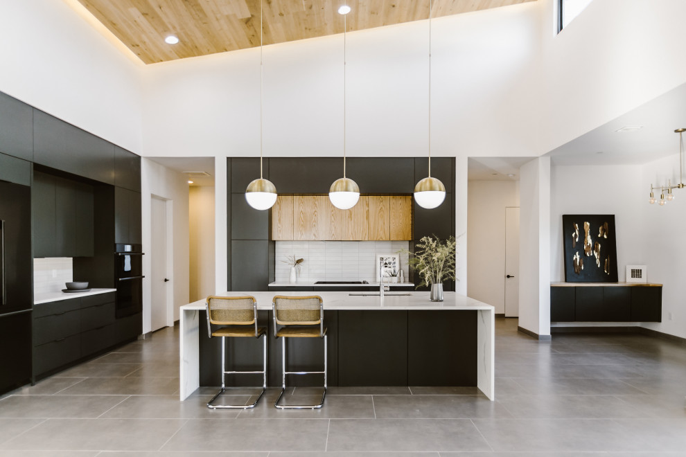 Large danish l-shaped porcelain tile and gray floor open concept kitchen photo in Other with an undermount sink, flat-panel cabinets, black cabinets, quartz countertops, white backsplash, porcelain backsplash, black appliances, an island and white countertops