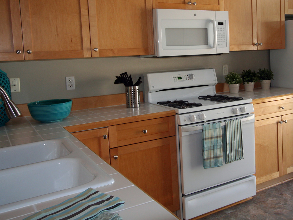 Esempio di una cucina a L design con lavello a doppia vasca, ante con riquadro incassato, ante in legno chiaro, top piastrellato e elettrodomestici bianchi