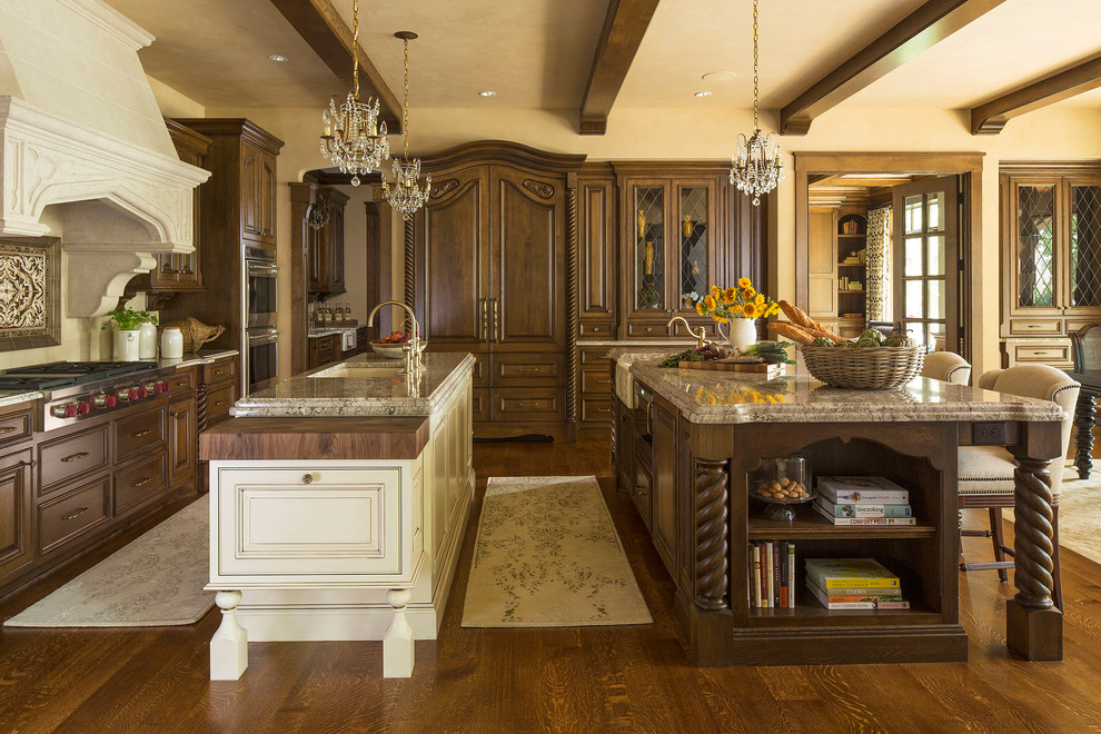 Cette image montre une cuisine américaine encastrable traditionnelle en L et bois brun avec un plan de travail en granite, un évier de ferme, une crédence beige et 2 îlots.