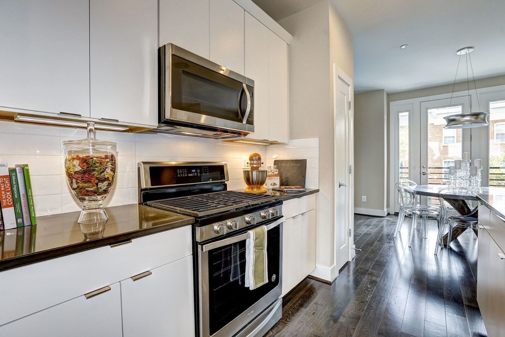 Example of a small trendy single-wall medium tone wood floor and brown floor eat-in kitchen design in Baltimore with an undermount sink, flat-panel cabinets, white cabinets, quartz countertops, white backsplash, subway tile backsplash, stainless steel appliances, an island and gray countertops