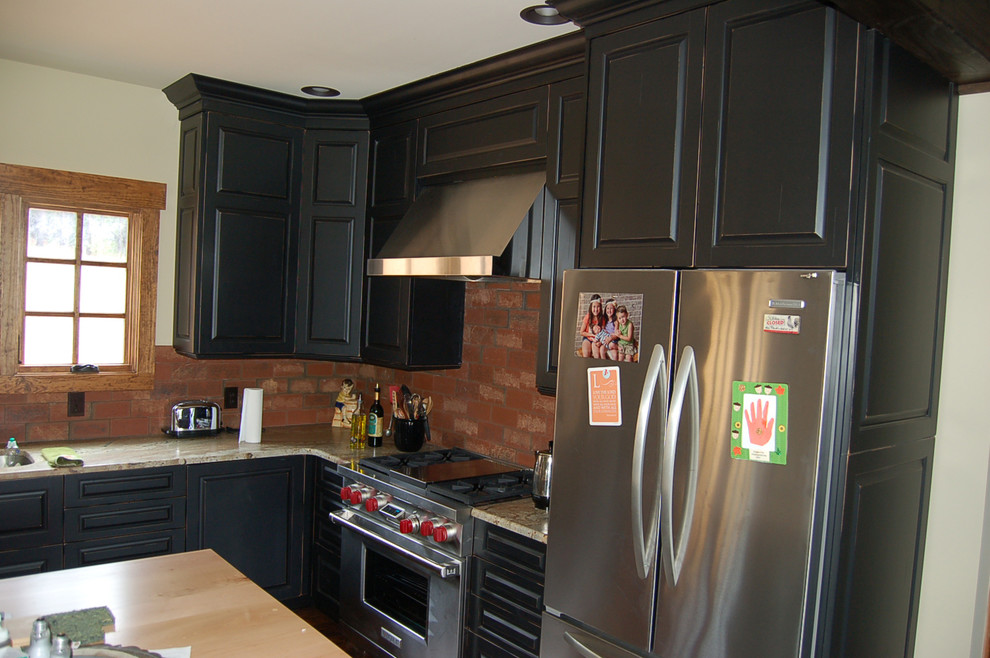 Bild på ett rustikt kök, med luckor med upphöjd panel, svarta skåp, rostfria vitvaror, en köksö, en undermonterad diskho, granitbänkskiva, rött stänkskydd och mörkt trägolv