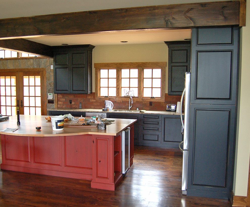 Inredning av ett rustikt kök, med luckor med upphöjd panel, svarta skåp, rostfria vitvaror, en köksö, en undermonterad diskho, granitbänkskiva, rött stänkskydd och mörkt trägolv