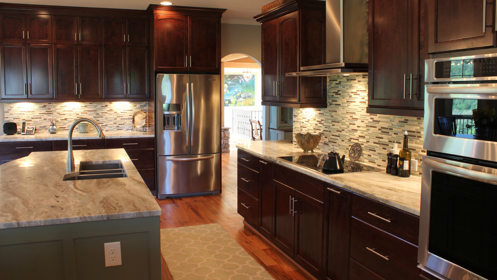 Inspiration pour une grande cuisine ouverte traditionnelle en bois foncé et L avec un placard avec porte à panneau encastré, un plan de travail en granite, une crédence multicolore, une crédence en carreau de verre, un électroménager en acier inoxydable, un sol en bois brun, îlot et un évier 3 bacs.