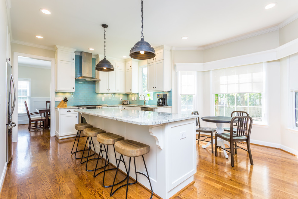 Example of a mid-sized transitional l-shaped medium tone wood floor eat-in kitchen design in Raleigh with an undermount sink, shaker cabinets, white cabinets, granite countertops, blue backsplash, glass tile backsplash, stainless steel appliances, an island and white countertops