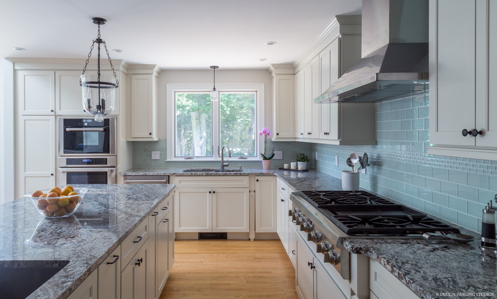 This is an example of a traditional l-shaped kitchen in Boston with shaker cabinets, white cabinets, blue splashback, glass tiled splashback, stainless steel appliances and an island.