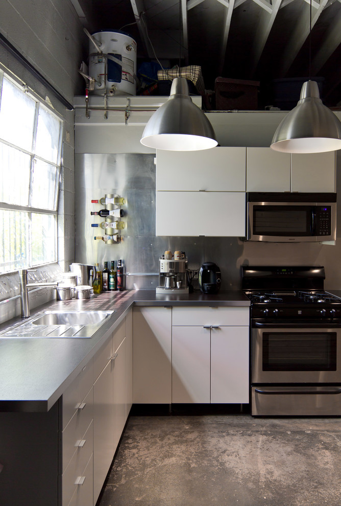 This is an example of an industrial l-shaped kitchen in Los Angeles with flat-panel cabinets, white cabinets and metallic splashback.