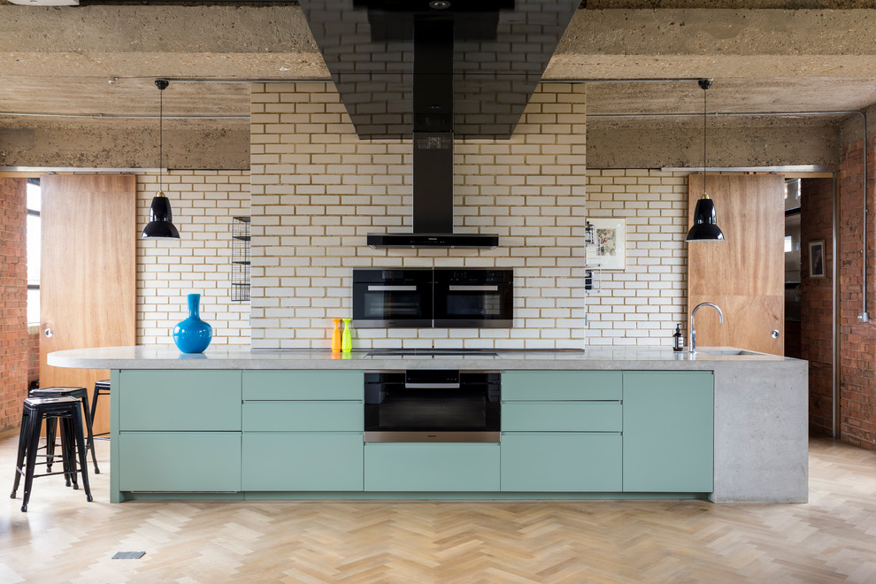 This is an example of an industrial single-wall kitchen in London with an integrated sink, flat-panel cabinets, turquoise cabinets, concrete worktops, white splashback, brick splashback, black appliances, light hardwood flooring, beige floors and grey worktops.