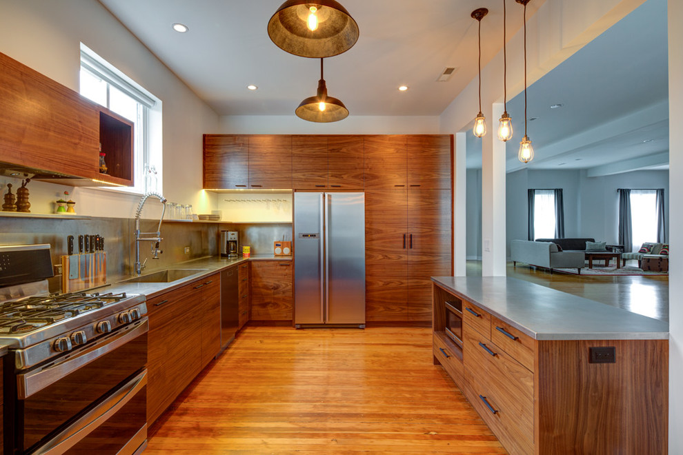 Offene Moderne Küche mit integriertem Waschbecken, flächenbündigen Schrankfronten, hellbraunen Holzschränken, Edelstahl-Arbeitsplatte, Küchenrückwand in Metallic, Küchengeräten aus Edelstahl, braunem Holzboden und Kücheninsel in Portland