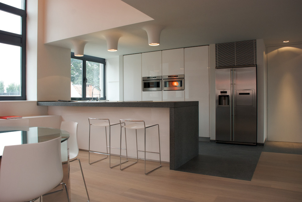 Foto de cocina comedor minimalista con electrodomésticos de acero inoxidable, armarios con paneles lisos y puertas de armario blancas