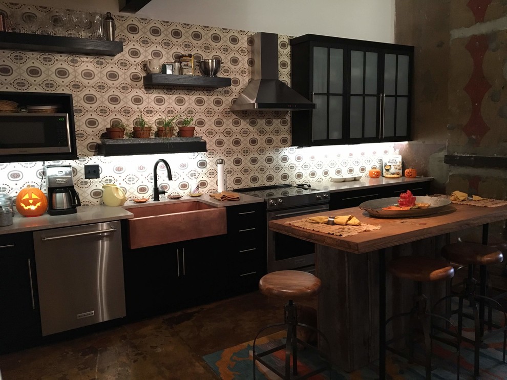 Diseño de cocina lineal industrial con fregadero sobremueble, armarios tipo vitrina, puertas de armario negras, encimera de mármol, salpicadero de azulejos de cemento, electrodomésticos de acero inoxidable, suelo de cemento, una isla, encimeras rosas y suelo marrón