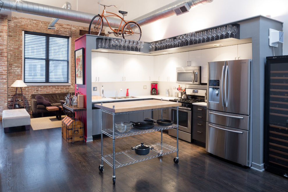 シカゴにある低価格の小さなインダストリアルスタイルのおしゃれなキッチン (フラットパネル扉のキャビネット、グレーのキャビネット、白いキッチンパネル、シルバーの調理設備、濃色無垢フローリング、ダブルシンク) の写真
