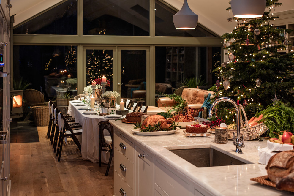 Example of a minimalist galley medium tone wood floor open concept kitchen design in Dublin with a farmhouse sink, glass-front cabinets, gray cabinets, marble countertops, white backsplash, ceramic backsplash, paneled appliances and an island