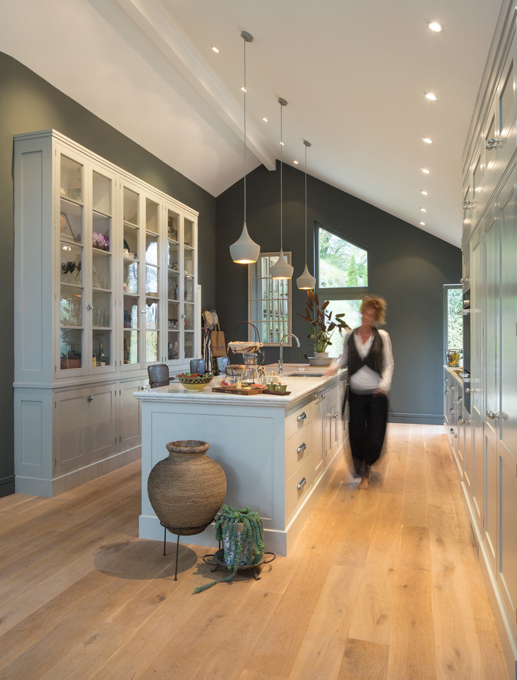 Inspiration for a modern galley open plan kitchen in Dublin with a belfast sink, glass-front cabinets, grey cabinets, marble worktops, white splashback, ceramic splashback, integrated appliances, medium hardwood flooring and an island.