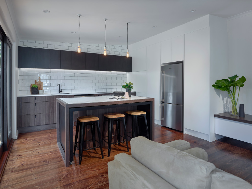 Photo of a large contemporary single-wall kitchen/diner in Other with a submerged sink, white splashback, ceramic splashback, stainless steel appliances, medium hardwood flooring, an island, flat-panel cabinets, dark wood cabinets, composite countertops and white worktops.