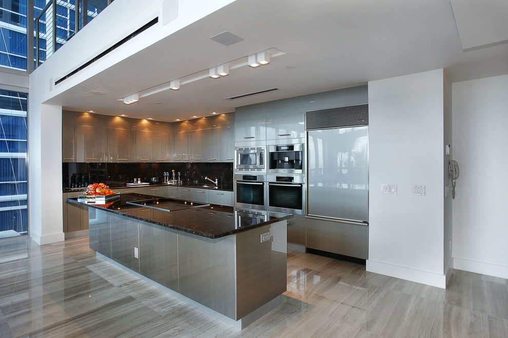 Contemporary l-shaped kitchen/diner in Miami with a submerged sink, flat-panel cabinets, marble worktops, black splashback, stone slab splashback and stainless steel appliances.