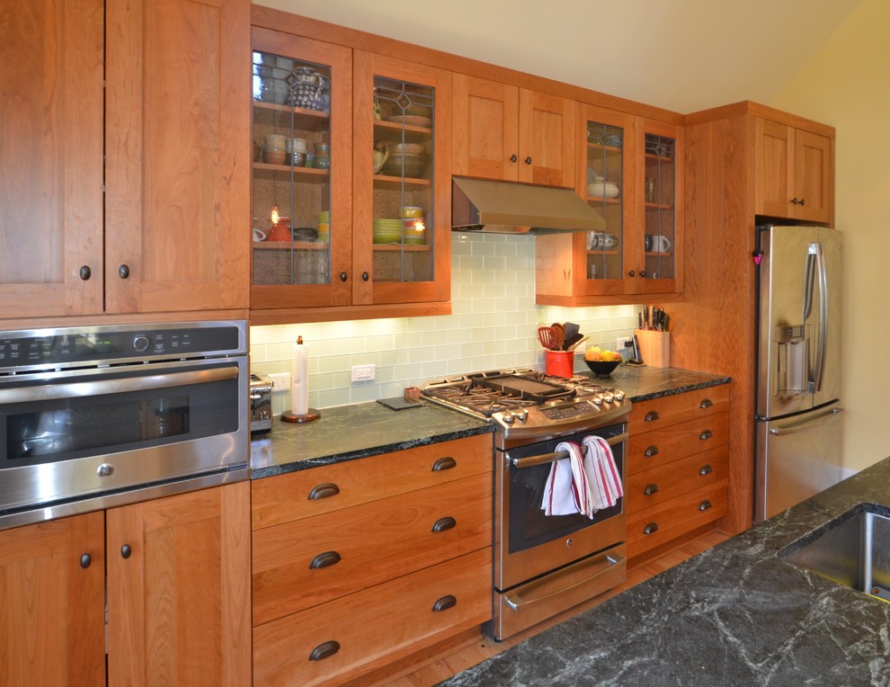 Exempel på ett mellanstort amerikanskt linjärt kök, med en undermonterad diskho, skåp i shakerstil, skåp i mellenmörkt trä, bänkskiva i täljsten, grått stänkskydd, stänkskydd i glaskakel, rostfria vitvaror, ljust trägolv, en köksö och brunt golv
