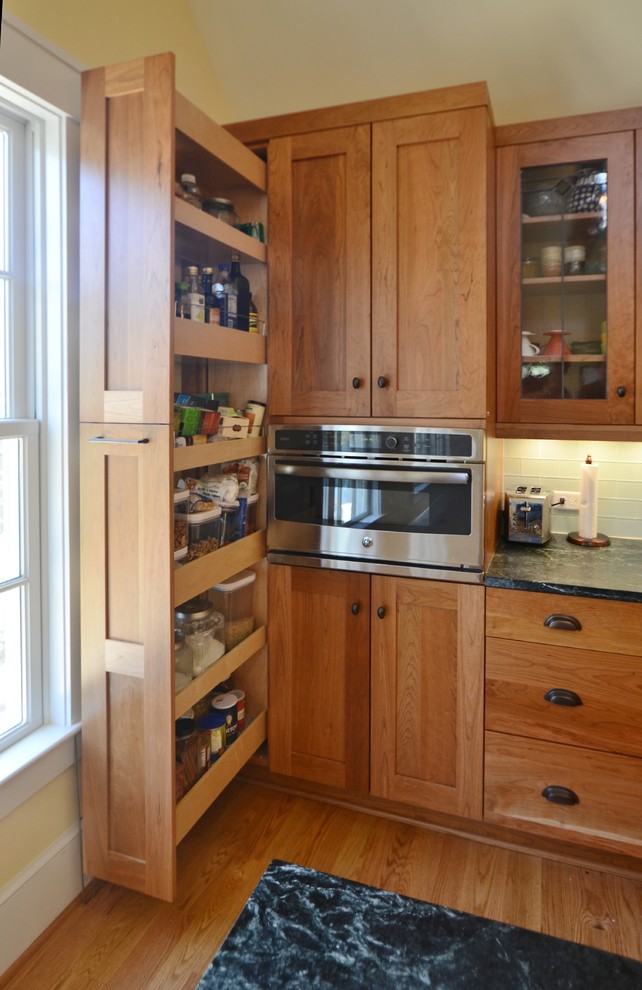 Foto på ett mellanstort amerikanskt linjärt kök, med en undermonterad diskho, skåp i shakerstil, skåp i mellenmörkt trä, bänkskiva i täljsten, grått stänkskydd, stänkskydd i glaskakel, rostfria vitvaror, ljust trägolv, en köksö och brunt golv