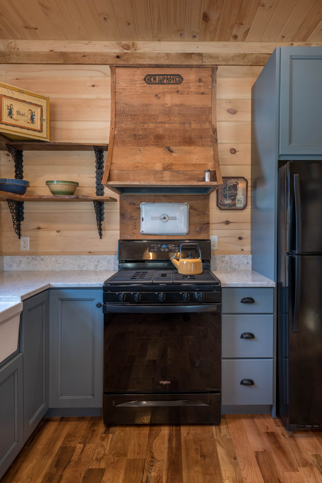 Photo of a small rustic u-shaped kitchen/diner in Minneapolis with a belfast sink, flat-panel cabinets, blue cabinets, engineered stone countertops, white splashback, black appliances, medium hardwood flooring, a breakfast bar, brown floors and white worktops.