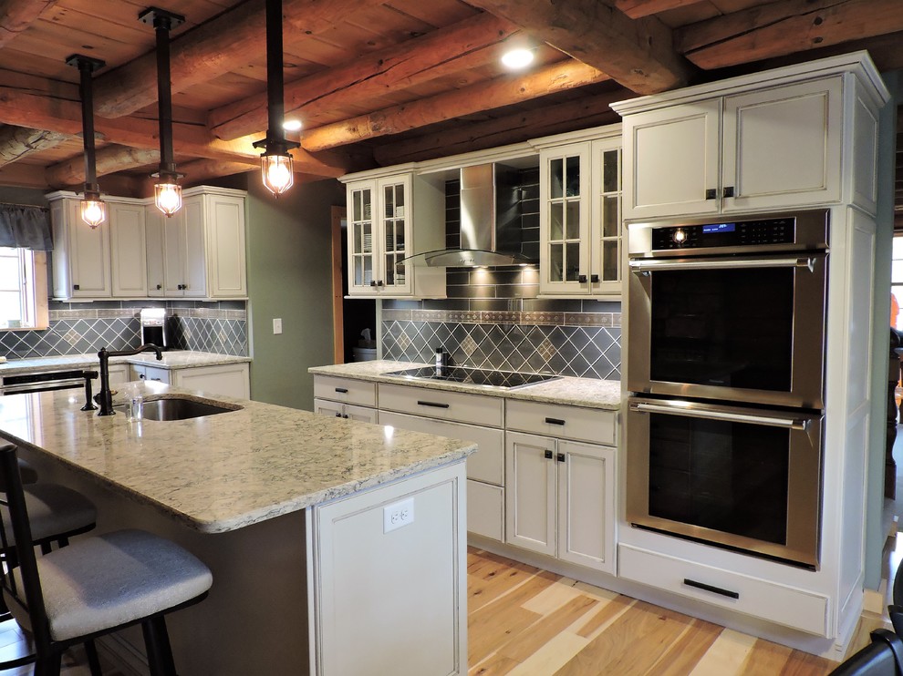 Foto på ett stort rustikt kök, med en undermonterad diskho, luckor med infälld panel, vita skåp, granitbänkskiva, grått stänkskydd, stänkskydd i porslinskakel, rostfria vitvaror, ljust trägolv och en köksö