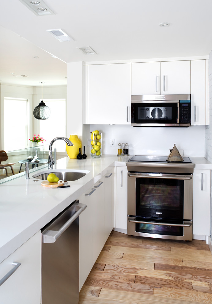 Bild på ett funkis kök, med en undermonterad diskho, släta luckor, vita skåp, rostfria vitvaror, bänkskiva i kvartsit, ljust trägolv, en halv köksö och beiget golv