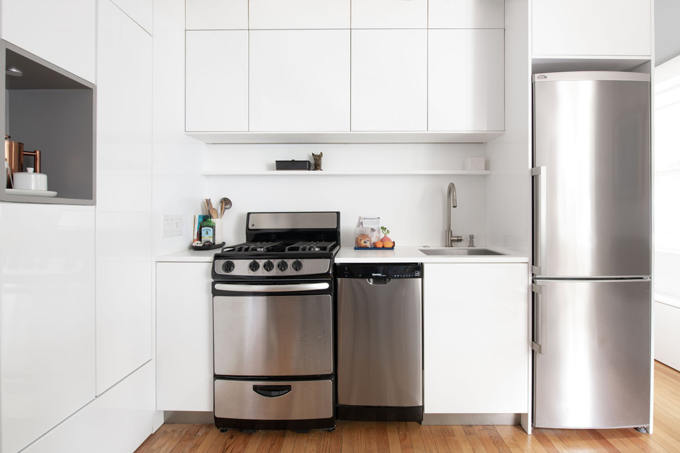 Exempel på ett litet modernt vit linjärt vitt kök med öppen planlösning, med en undermonterad diskho, släta luckor, vita skåp, bänkskiva i koppar, vitt stänkskydd, rostfria vitvaror, ljust trägolv och beiget golv