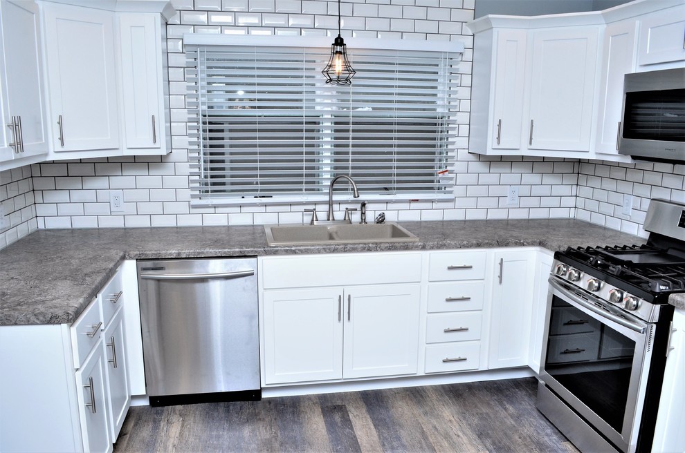 Example of a mid-sized transitional u-shaped light wood floor and gray floor enclosed kitchen design in Other with a drop-in sink, shaker cabinets, white cabinets, laminate countertops, white backsplash, subway tile backsplash, stainless steel appliances, no island and gray countertops