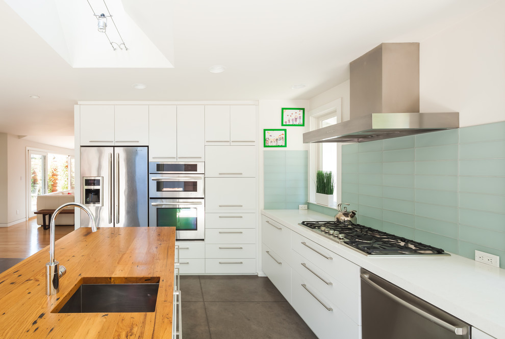 Moderne Küche in L-Form mit flächenbündigen Schrankfronten, weißen Schränken, Arbeitsplatte aus Holz, Küchenrückwand in Blau, Rückwand aus Glasfliesen, Küchengeräten aus Edelstahl und Kücheninsel in San Francisco