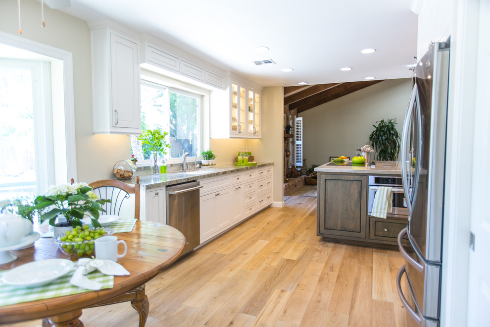 Inredning av ett modernt stort linjärt kök och matrum, med en undermonterad diskho, skåp i shakerstil, vita skåp, granitbänkskiva, rostfria vitvaror, mellanmörkt trägolv, en köksö, grått stänkskydd och beiget golv