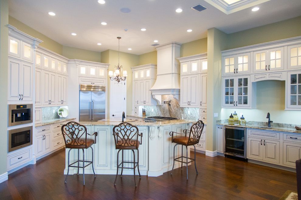 Large tuscan l-shaped dark wood floor and brown floor enclosed kitchen photo in Orlando with an undermount sink, raised-panel cabinets, white cabinets, granite countertops, multicolored backsplash, stone slab backsplash, stainless steel appliances and an island