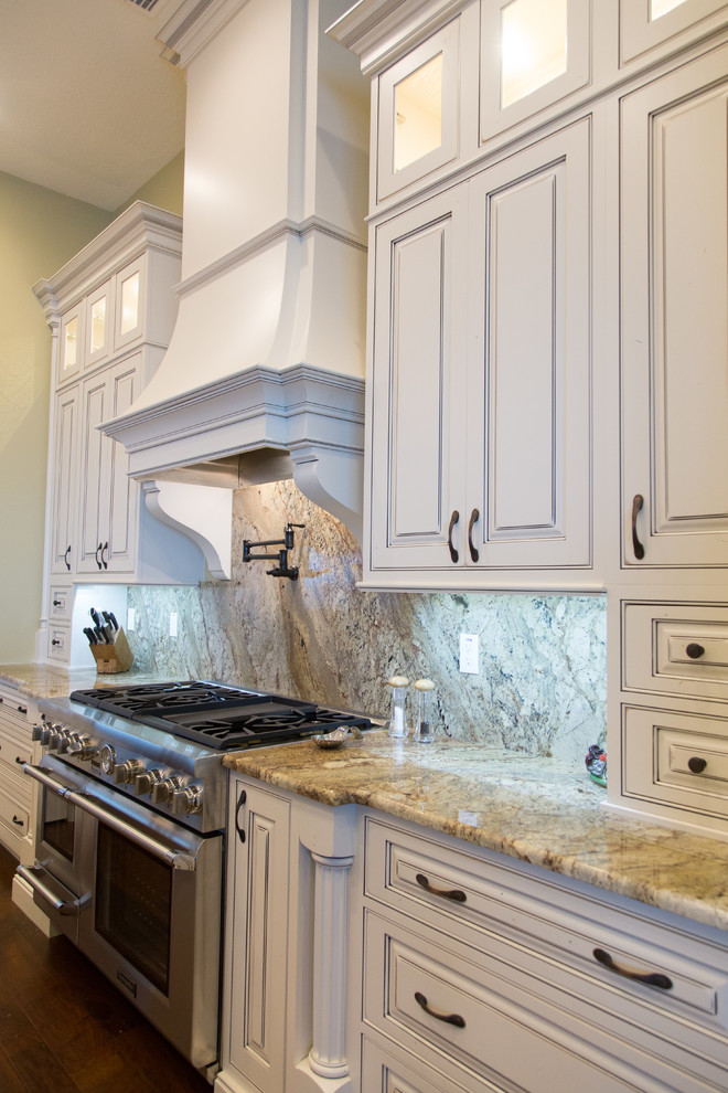 Foto på ett avskilt, stort medelhavsstil l-kök, med en undermonterad diskho, luckor med upphöjd panel, vita skåp, granitbänkskiva, flerfärgad stänkskydd, stänkskydd i sten, rostfria vitvaror, mörkt trägolv och en köksö