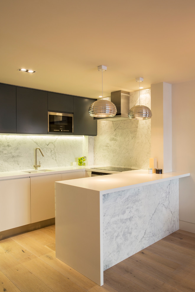 Inspiration for a contemporary u-shaped kitchen in London with a double-bowl sink, flat-panel cabinets, white splashback, stainless steel appliances, light hardwood flooring and a breakfast bar.