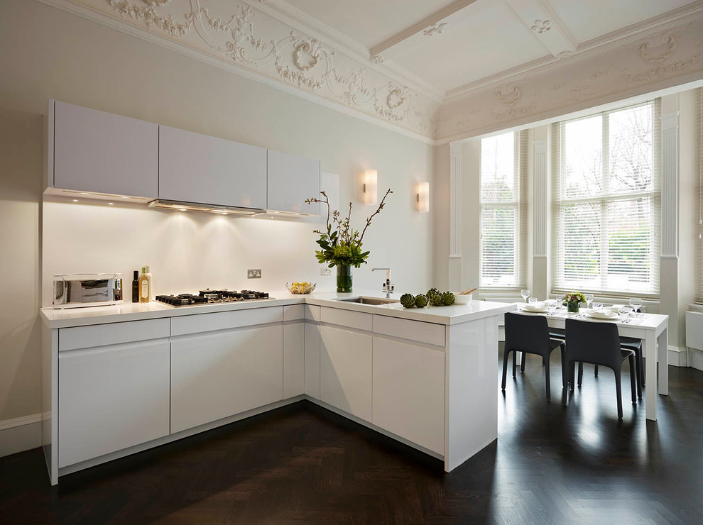 Contemporary kitchen/diner in London with a submerged sink, flat-panel cabinets, white cabinets, white splashback, dark hardwood flooring and a breakfast bar.