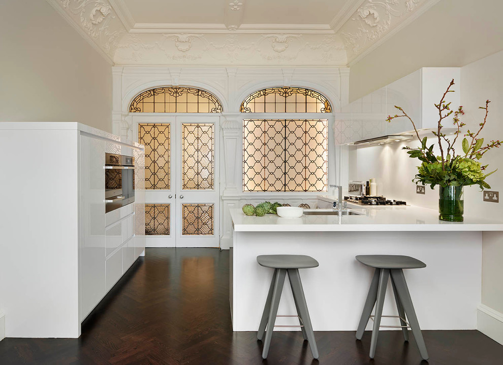 Contemporary u-shaped kitchen in London with a submerged sink, flat-panel cabinets, white cabinets, white splashback, dark hardwood flooring and a breakfast bar.