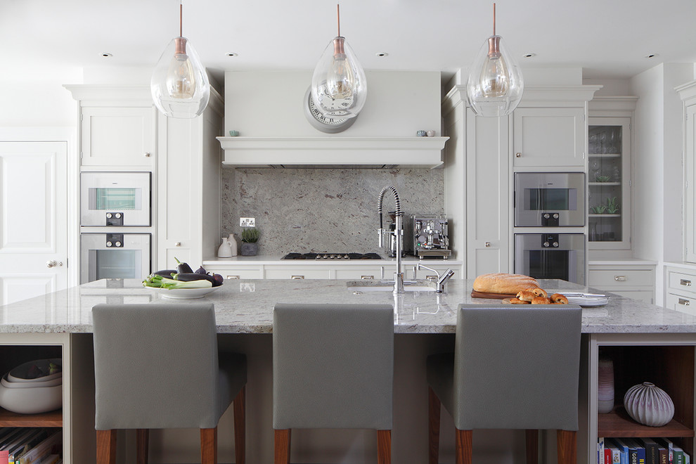 Traditional kitchen in London with a submerged sink, shaker cabinets, white cabinets, grey splashback, stainless steel appliances, an island and grey worktops.