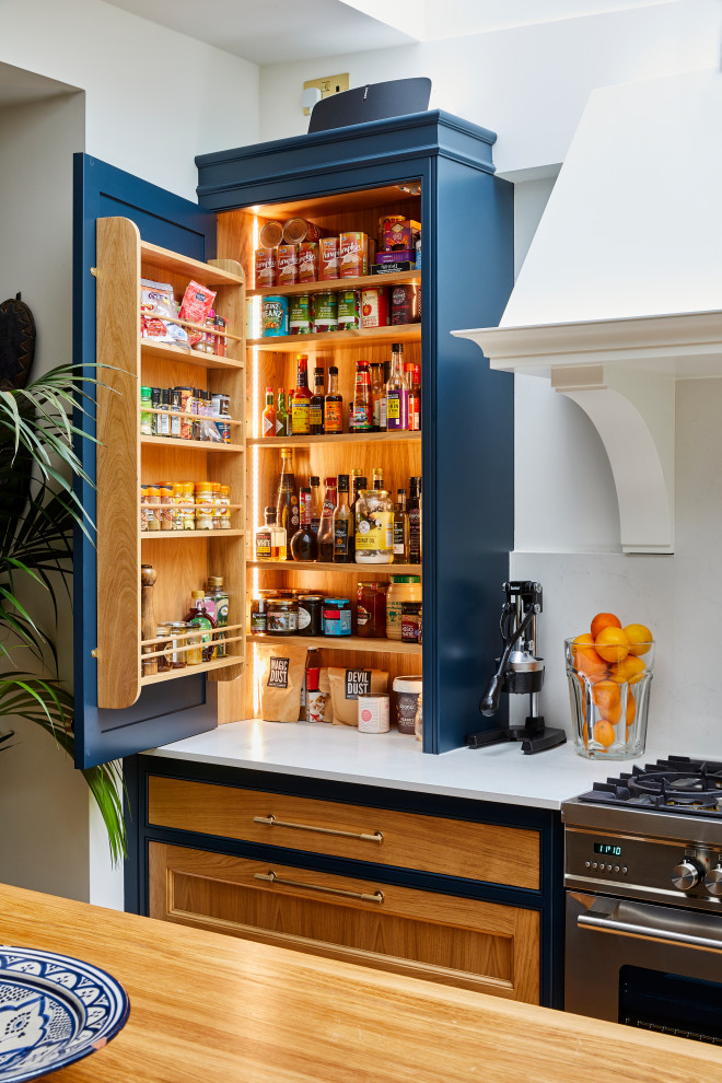 This is an example of a large traditional galley open plan kitchen in London with a belfast sink, shaker cabinets, blue cabinets, quartz worktops, grey splashback, stone slab splashback, stainless steel appliances, dark hardwood flooring, an island, brown floors and grey worktops.