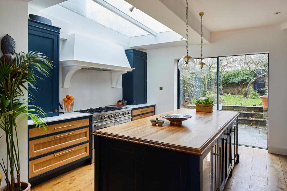 This is an example of a large traditional galley open plan kitchen in London with a belfast sink, shaker cabinets, blue cabinets, quartz worktops, grey splashback, stone slab splashback, stainless steel appliances, dark hardwood flooring, an island, brown floors and grey worktops.