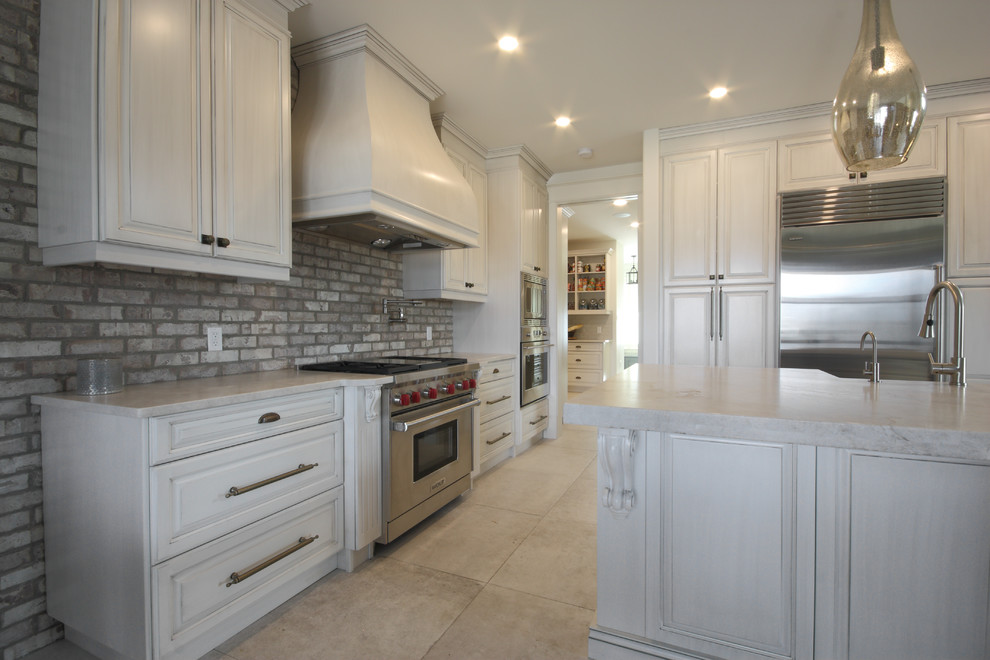 Inspiration for a large traditional l-shaped kitchen/diner in Calgary with raised-panel cabinets, white cabinets, engineered stone countertops, stainless steel appliances, an island, a belfast sink, grey splashback and brick splashback.