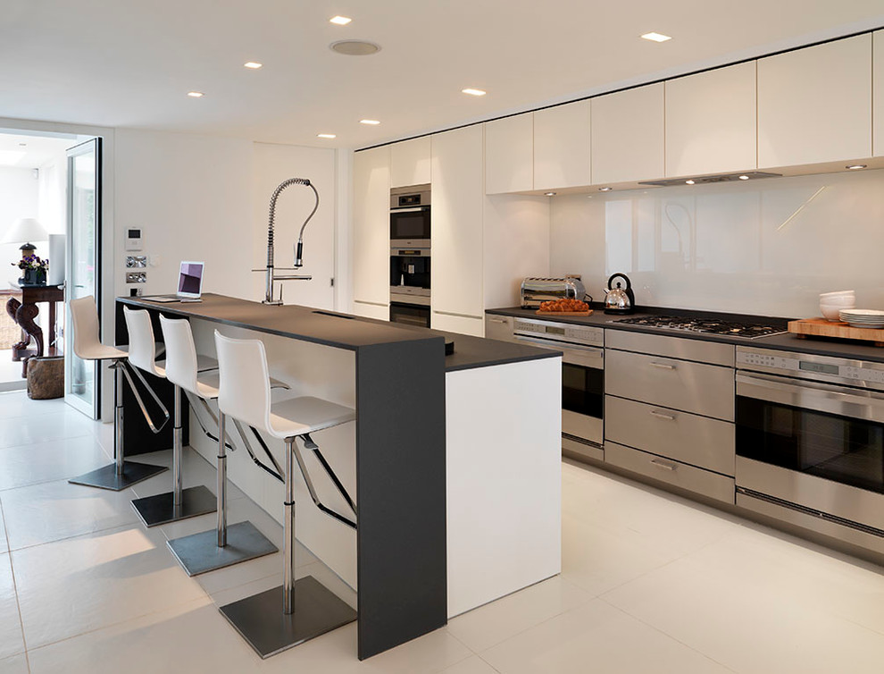 Kitchen - contemporary kitchen idea in London with flat-panel cabinets, stainless steel appliances and black countertops
