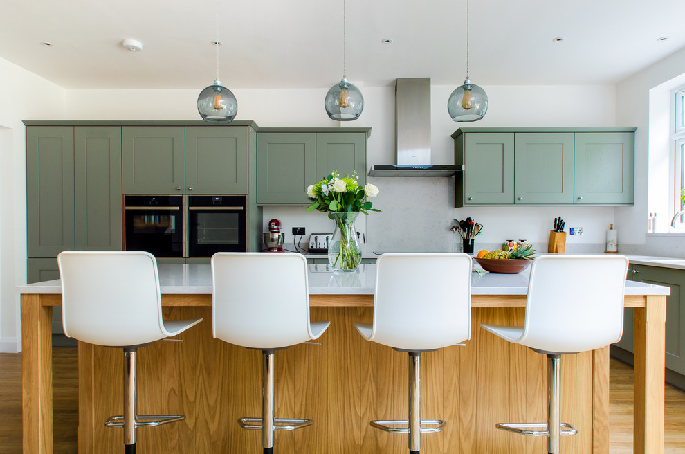 Inspiration for a large classic kitchen in Kent with shaker cabinets, green cabinets, white splashback, stainless steel appliances, medium hardwood flooring, an island and brown floors.