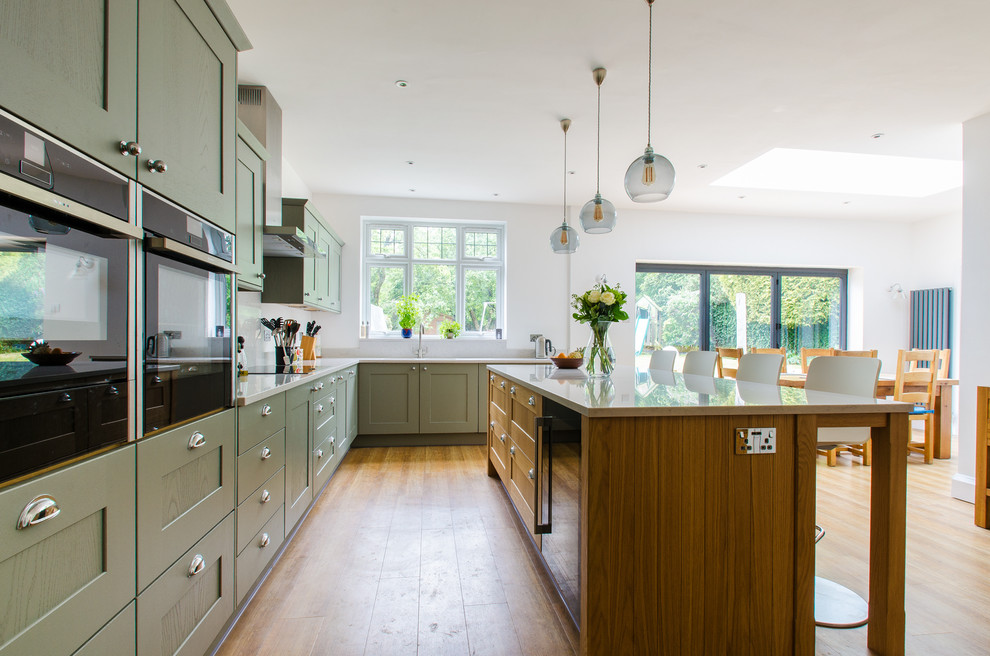 Large traditional kitchen in Kent with shaker cabinets, quartz worktops, green cabinets, light hardwood flooring, a breakfast bar and beige floors.