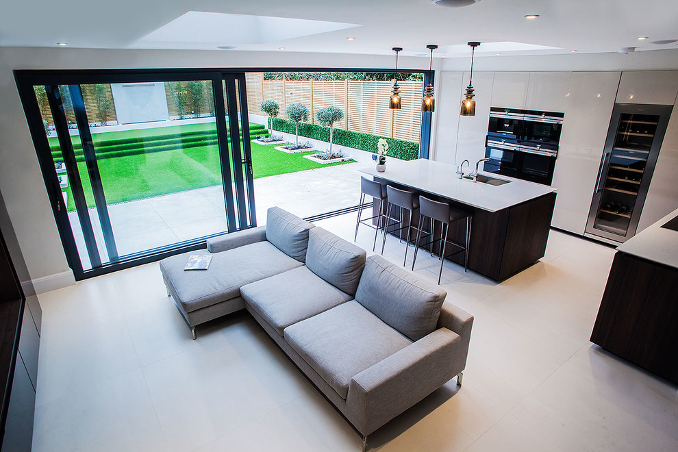 Large contemporary l-shaped open plan kitchen in London with an integrated sink, flat-panel cabinets, white cabinets, engineered stone countertops, mirror splashback, integrated appliances, porcelain flooring and an island.
