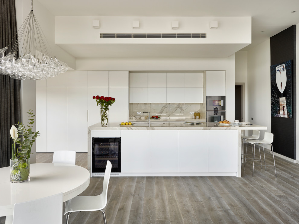 Modern inredning av ett mellanstort linjärt kök med öppen planlösning, med en dubbel diskho, släta luckor, vita skåp, marmorbänkskiva, vitt stänkskydd, stänkskydd i sten, rostfria vitvaror och en köksö