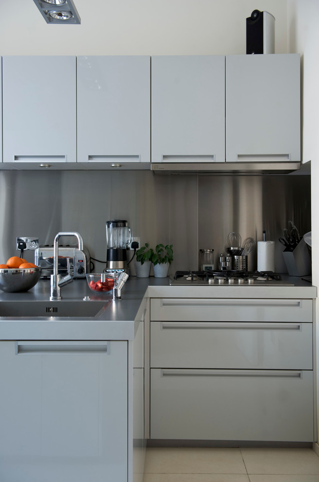 This is an example of a medium sized contemporary l-shaped kitchen in London with an integrated sink, flat-panel cabinets, stainless steel worktops, metallic splashback and porcelain flooring.