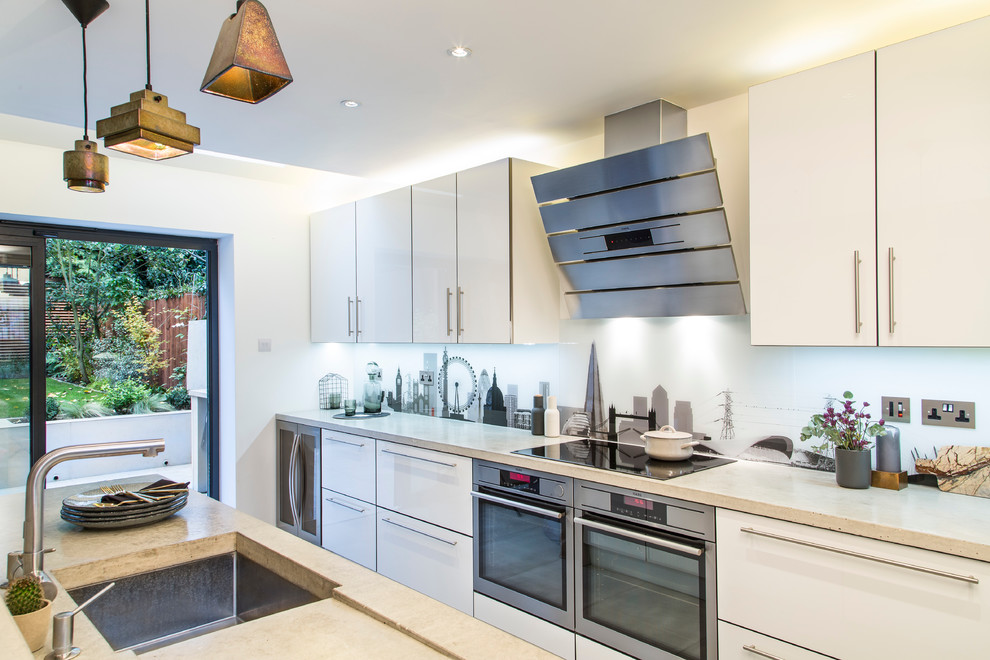 This is an example of a medium sized contemporary single-wall kitchen/diner in London with a submerged sink, flat-panel cabinets, white cabinets, concrete worktops, multi-coloured splashback, glass sheet splashback, stainless steel appliances, porcelain flooring and an island.